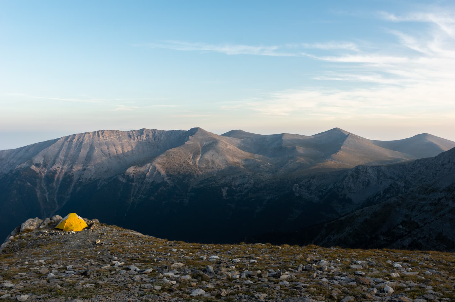 yellow tens next to a cliff with the peaks of south Olympus in the background